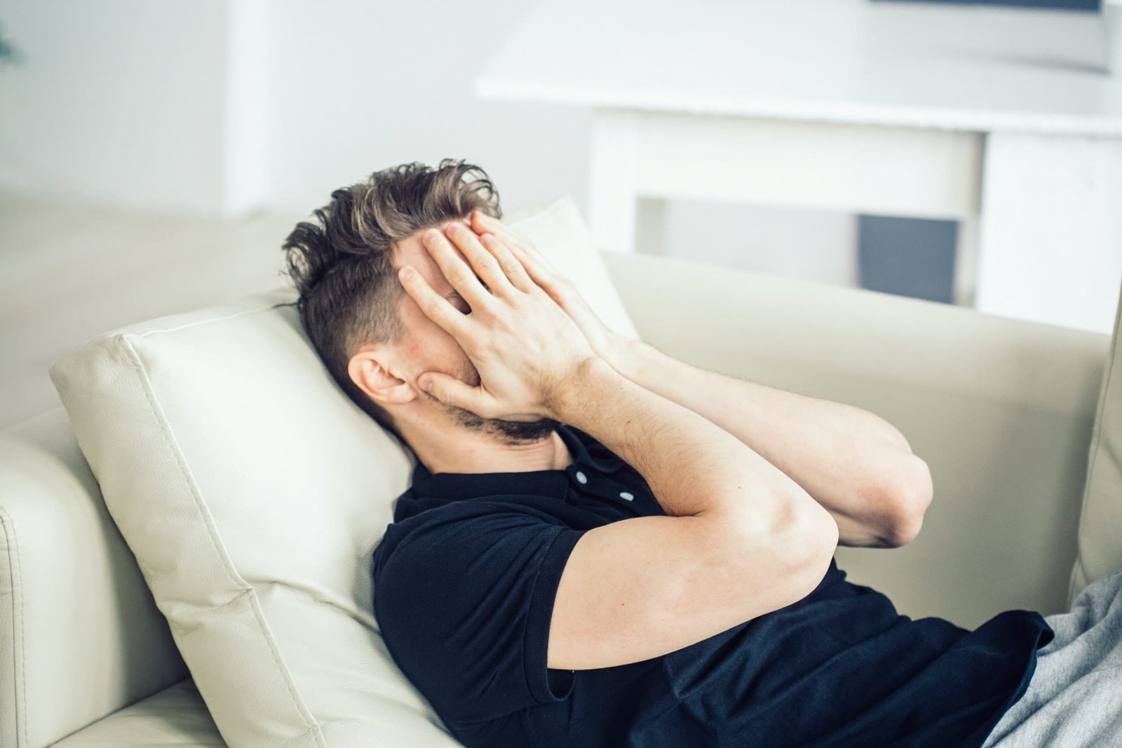 Headache. Handsome man problems stress sitting home alone on sofe hands cover head. Depression