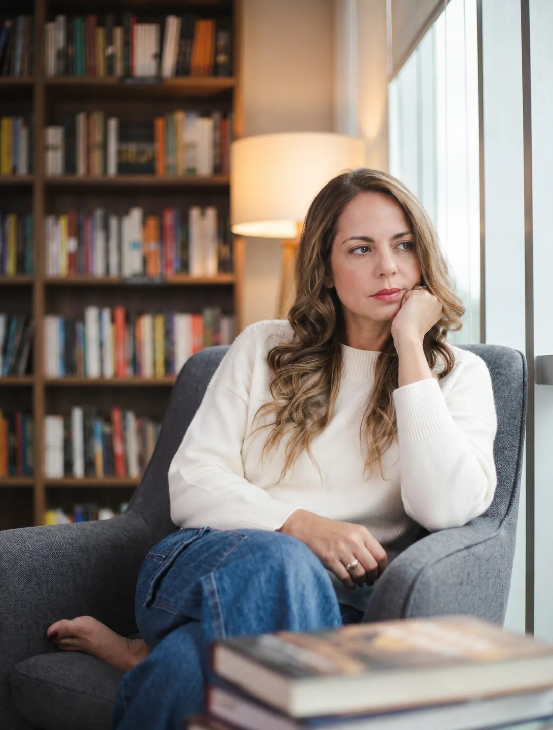 Maggie Pulido sentada en un sillón frente a una biblioteca, mirando hacia la ventana